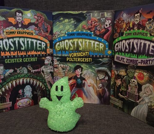 Drei Bücher der Ghostsitter-Reihe mit gezeichneten Covers, und davor steht ein kleiner, neongrüner Plastikgeist